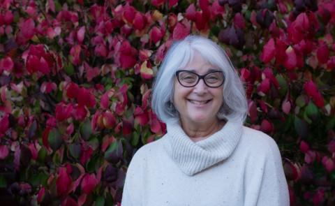 Photo of Shelley Cohen Konrad in white against a background of red leaves. 